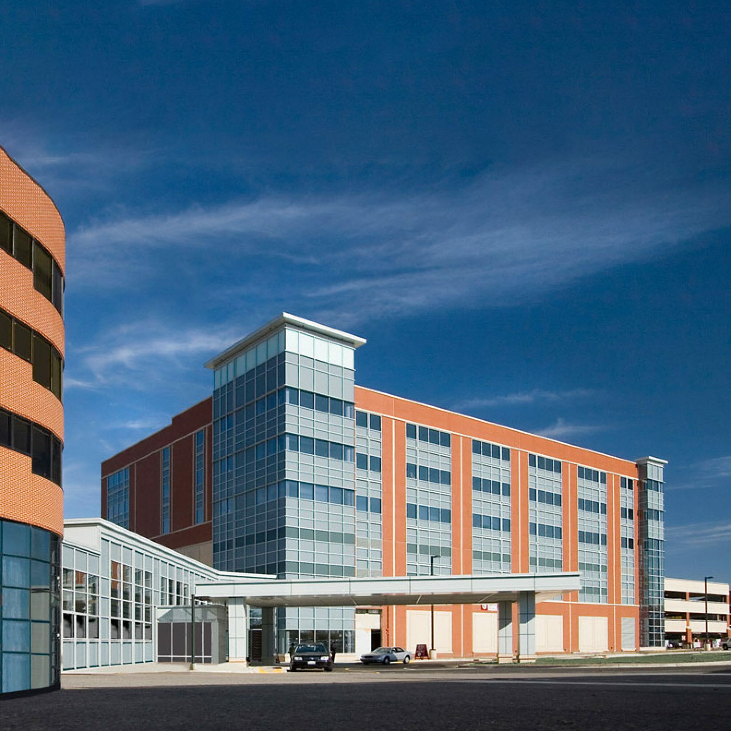 Exterior of multi-story brick and glass medical building with a porte-cochère and two cars under it