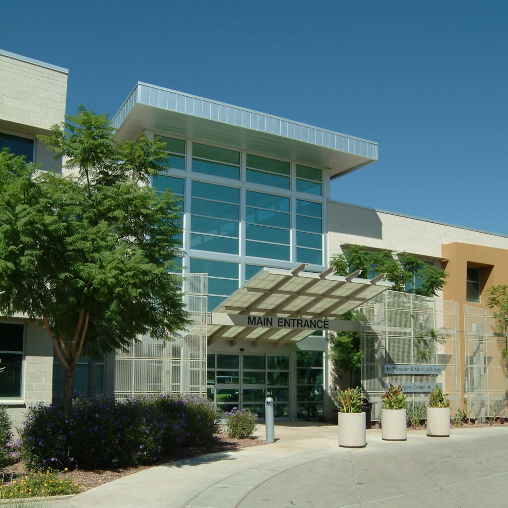 Exterior of main entrance of a two-story medical building with trees and flowers lining the exterior of the tan and orange building