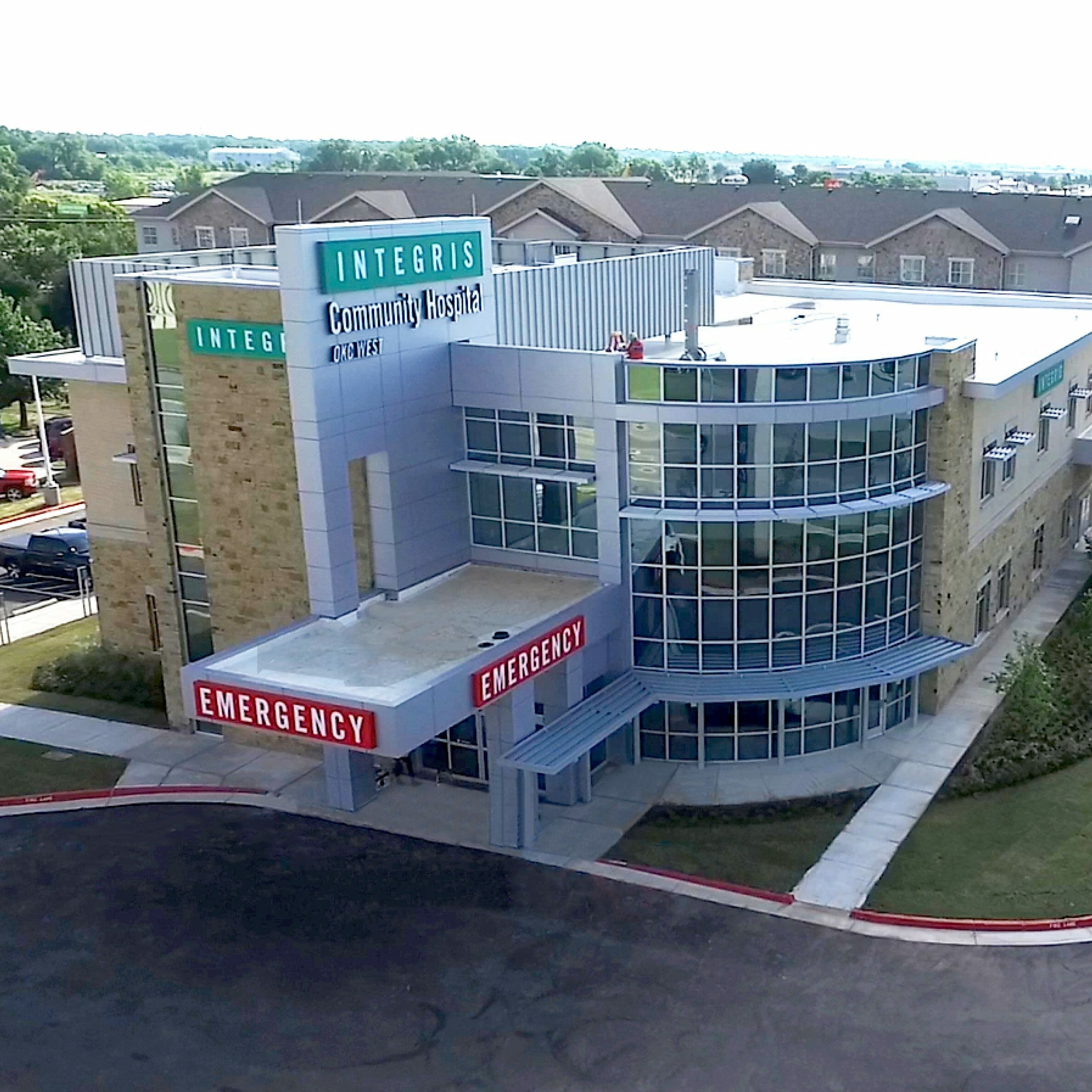 Aerial view of Integris OKC West community hospital, showing the red emergency sign with white letters and the teal integris sign on top.