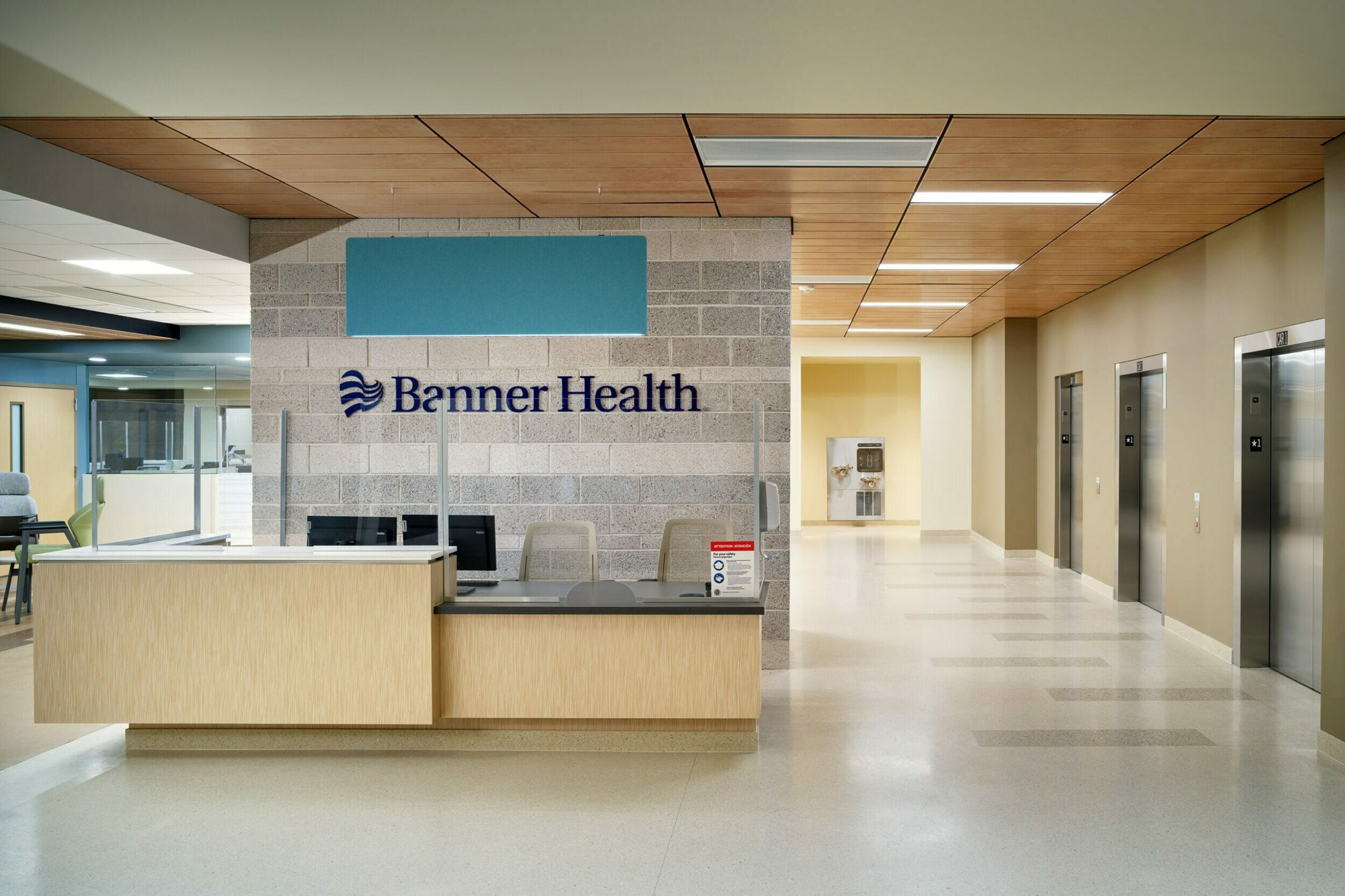 The front desk at Banner Health Center plus with gray stone background behind the desk with the Banner Health logo and name on it, with a light tan desk and wood ceilings