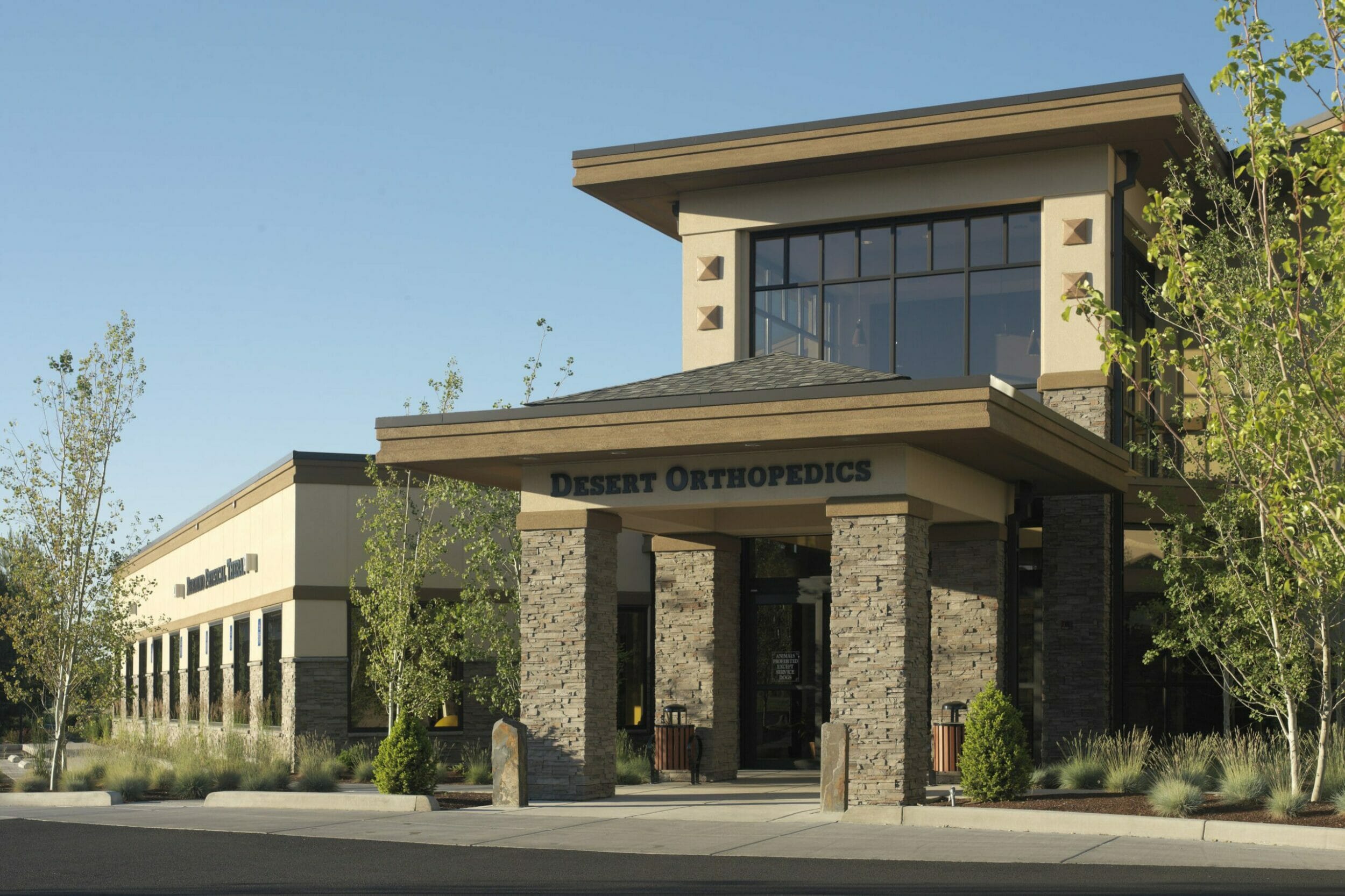 Exterior close-up daytime shot of the entrance to Bend Surgery Center with the Desert Orthopedics sign above the entrance and plants surrounding the building