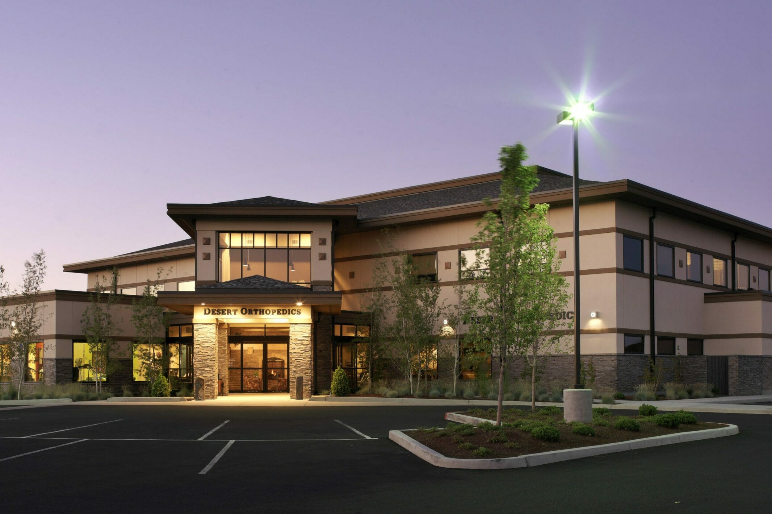 Exterior of Bend Surgery Center at night with accents of stone at the bottom of the building and a tan, stucco exterior