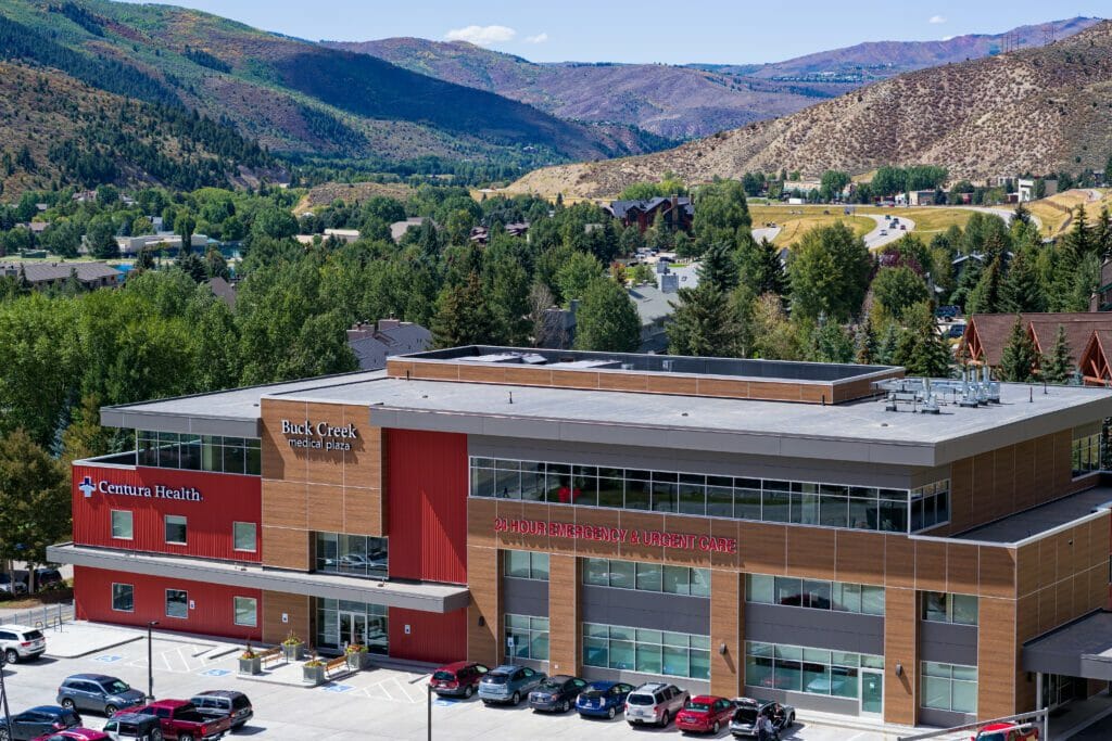 Aerial view of a 3-story medical center with a red and wood exterior with mountainous background