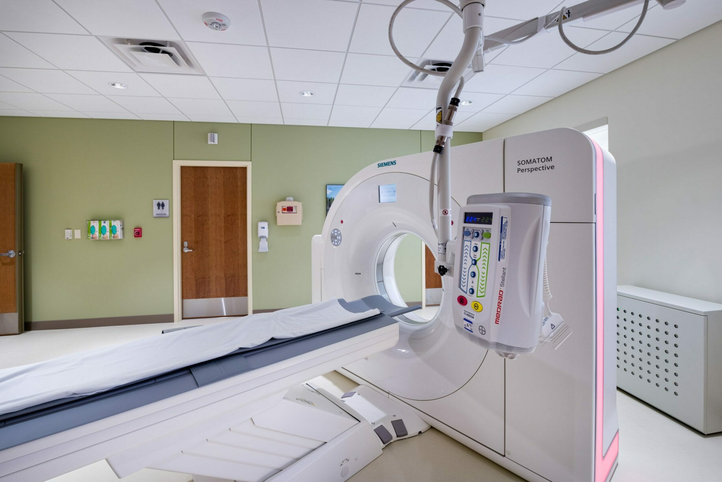 Medical office room with a SOMATOM Perspective CT Scanner and a light green accent wall with white floors