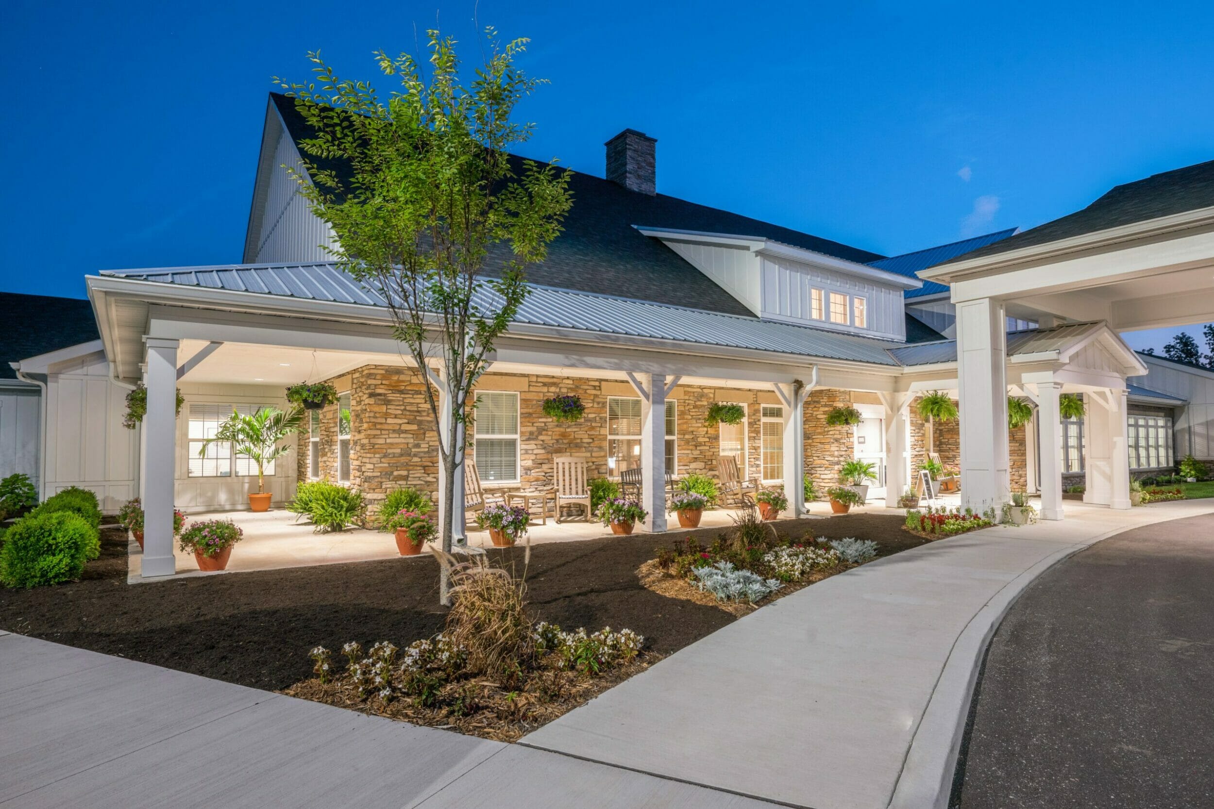 Exterior view of Demaree Crossing senior living at dusk with lit outdoor patio and porte corchere