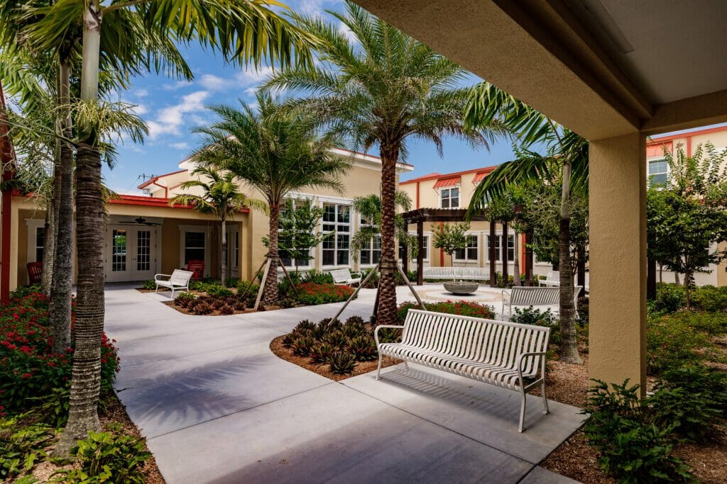 Courtyard of yellow exterior The Gallery at Cape Coral with white bench and palm trees
