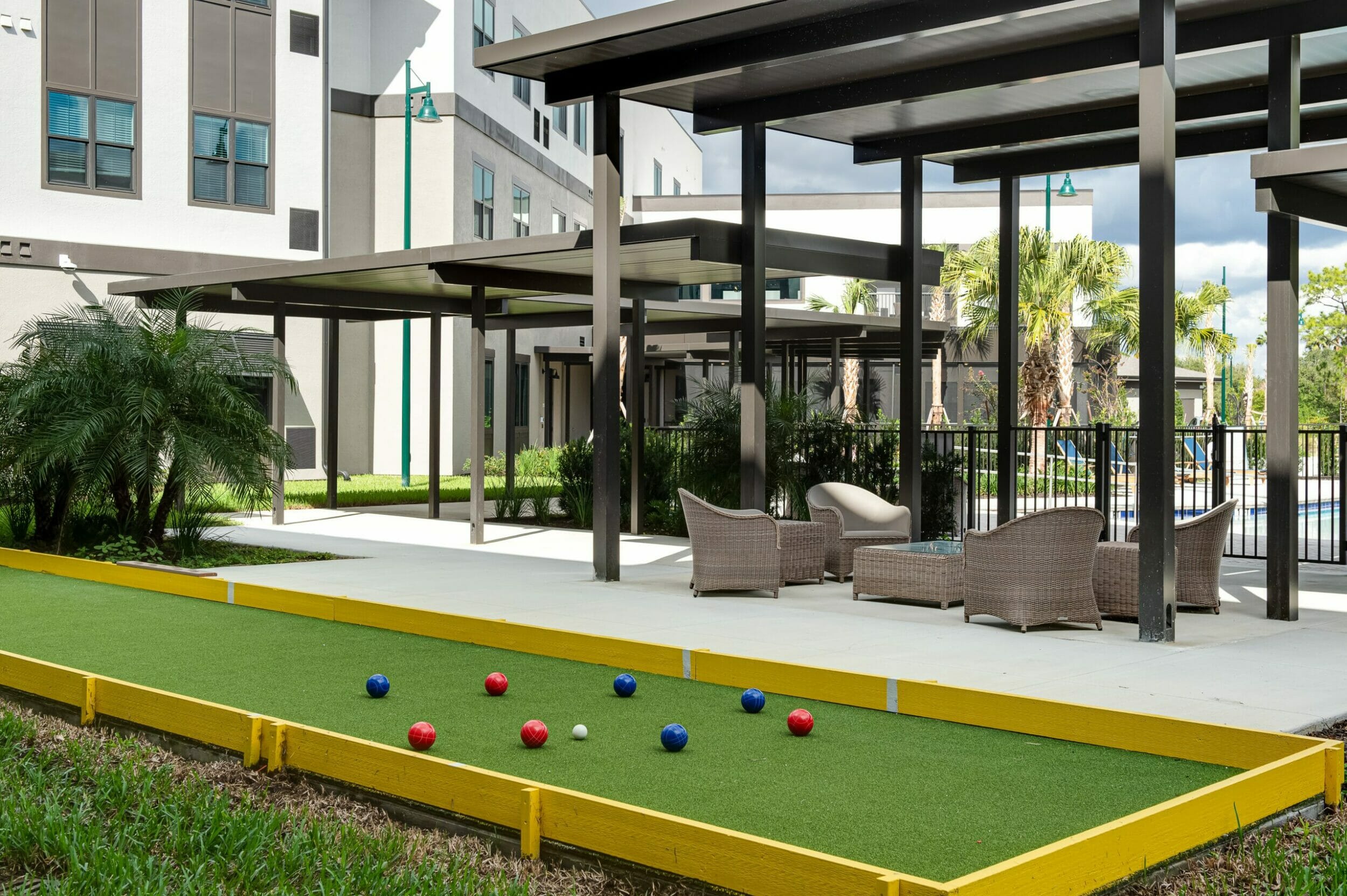 outdoor patio with bocce ball court and lounge area with a view of the pool on the other side of the fence