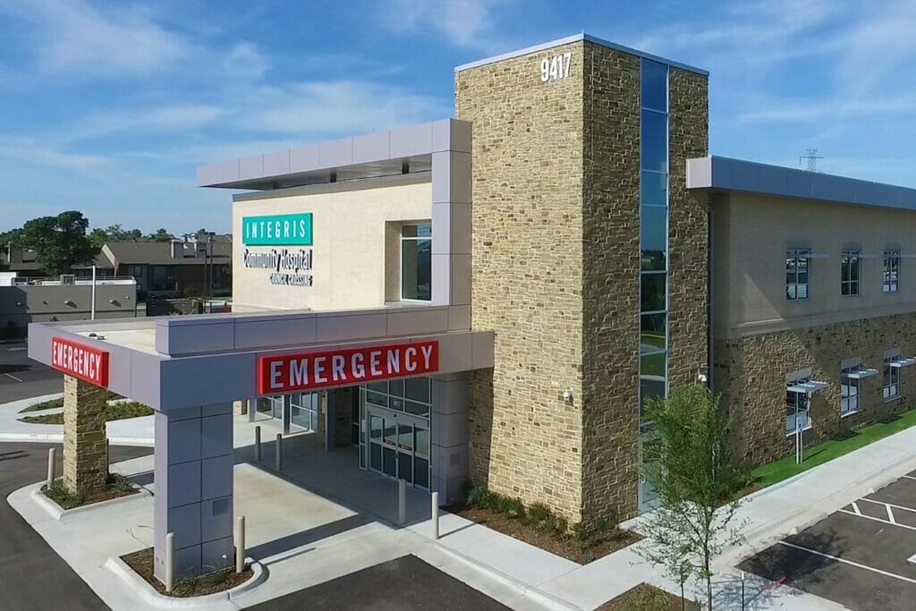 Side view of Integris OKC West community hospital, showing the red emergency sign with white letters and the teal integris sign on top.