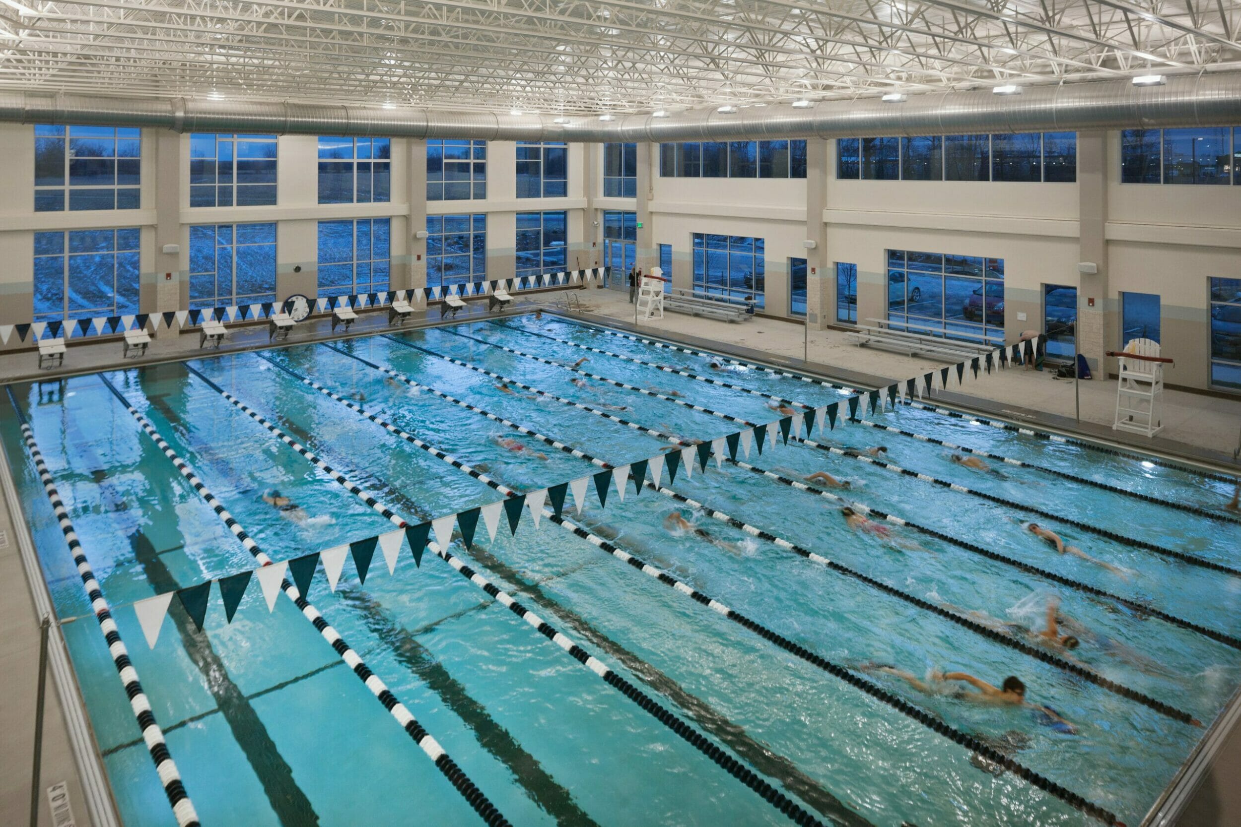 two-story lap pool with blue and white accent lanes and flags inside wellness center with several people swimming