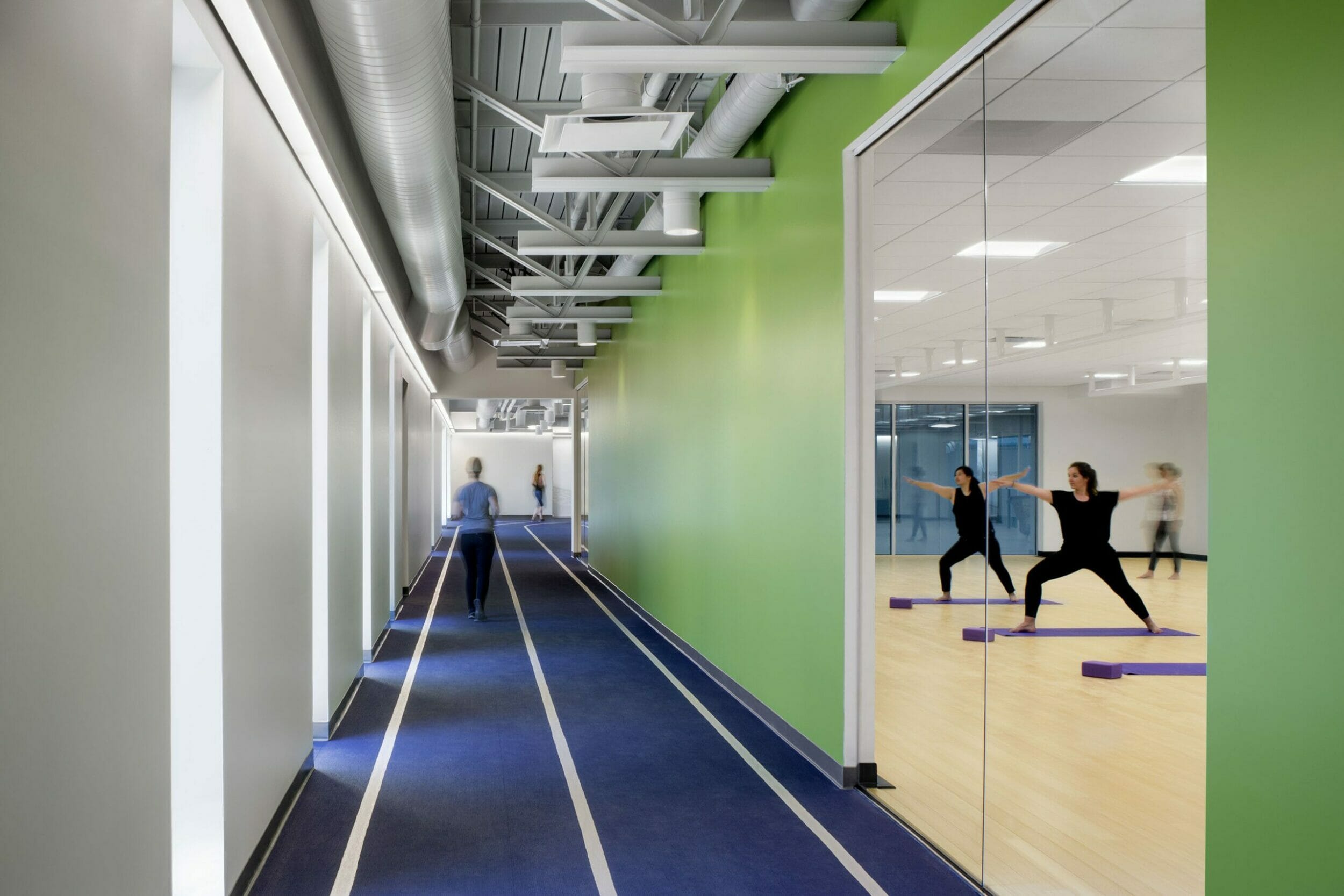Blue running circle inside wellness center with white and green accent walls with a glass door where you can see inside a yoga class