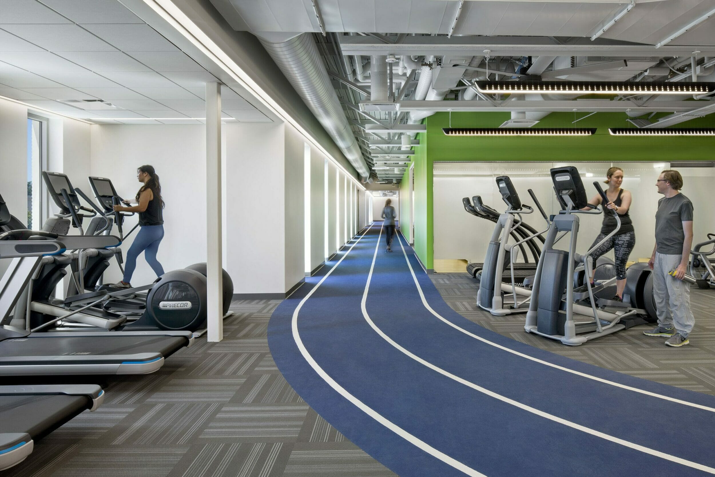 People working out on precor workout machines on either side of a blue running track inside a wellness center