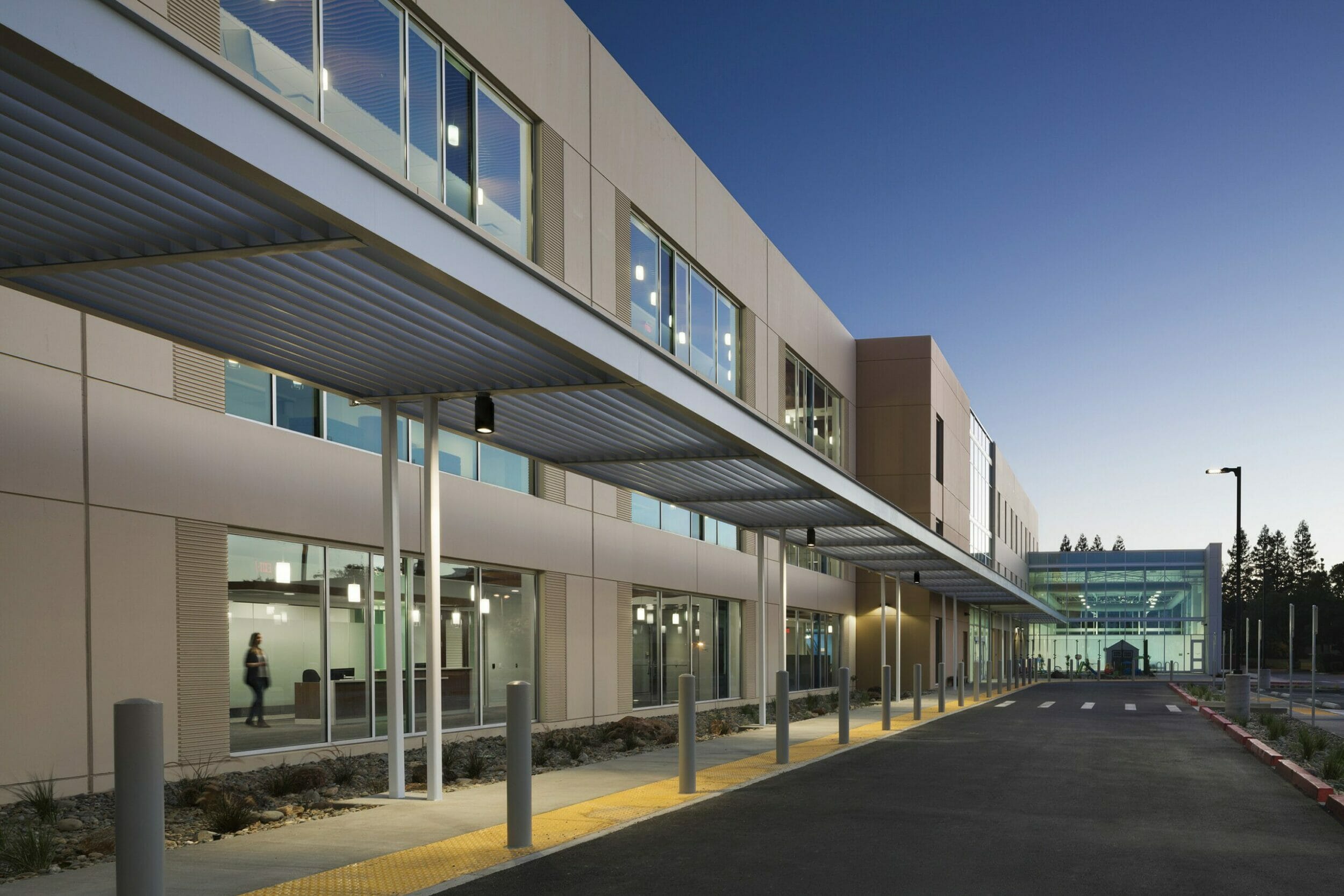 Close-up of exterior of medical building with gray metal awning over walkway to all glass section of building