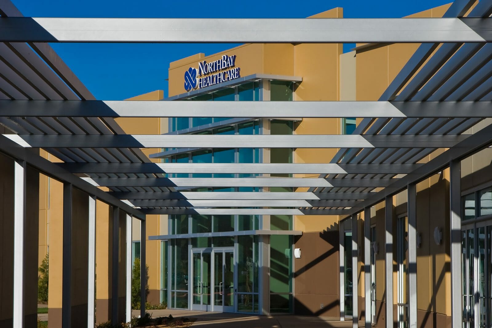 Exterior of NorthBay Healthcare with orange and brown exterior on the path to the front entrance under the pergola
