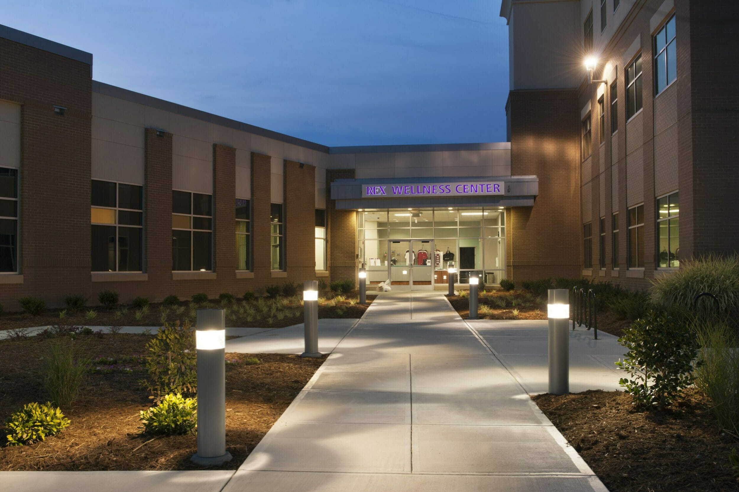 Exterior view of REX wellness center at night with lights leading up to the glass, front door