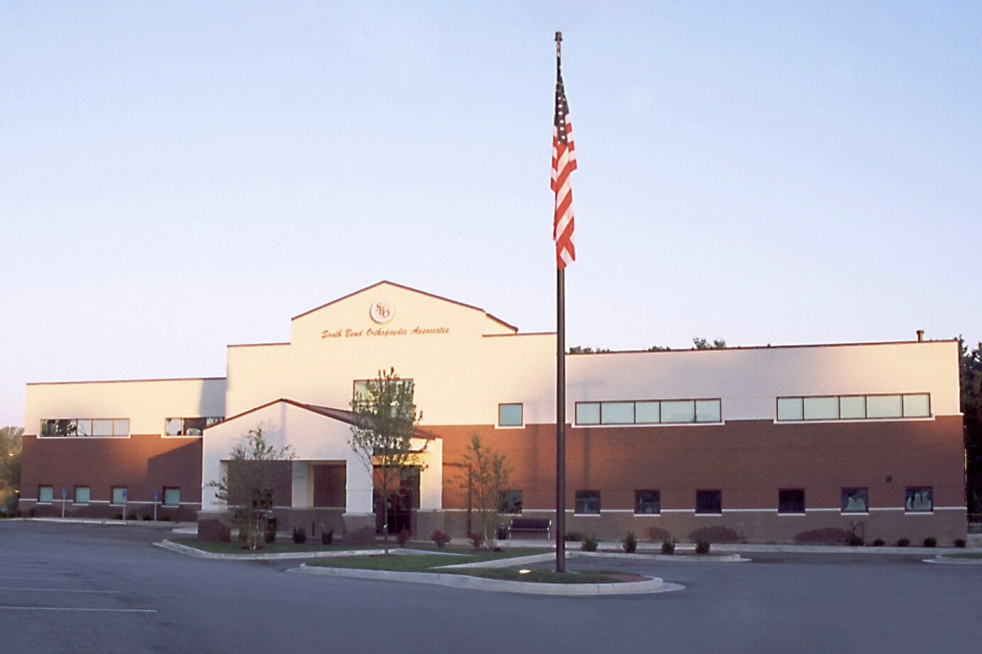 Exterior front view of the two-story, South Bend Orthopedic Associates building with stucco and brick finishes, a porte-cochère, and tall flag pole with the American flag on it