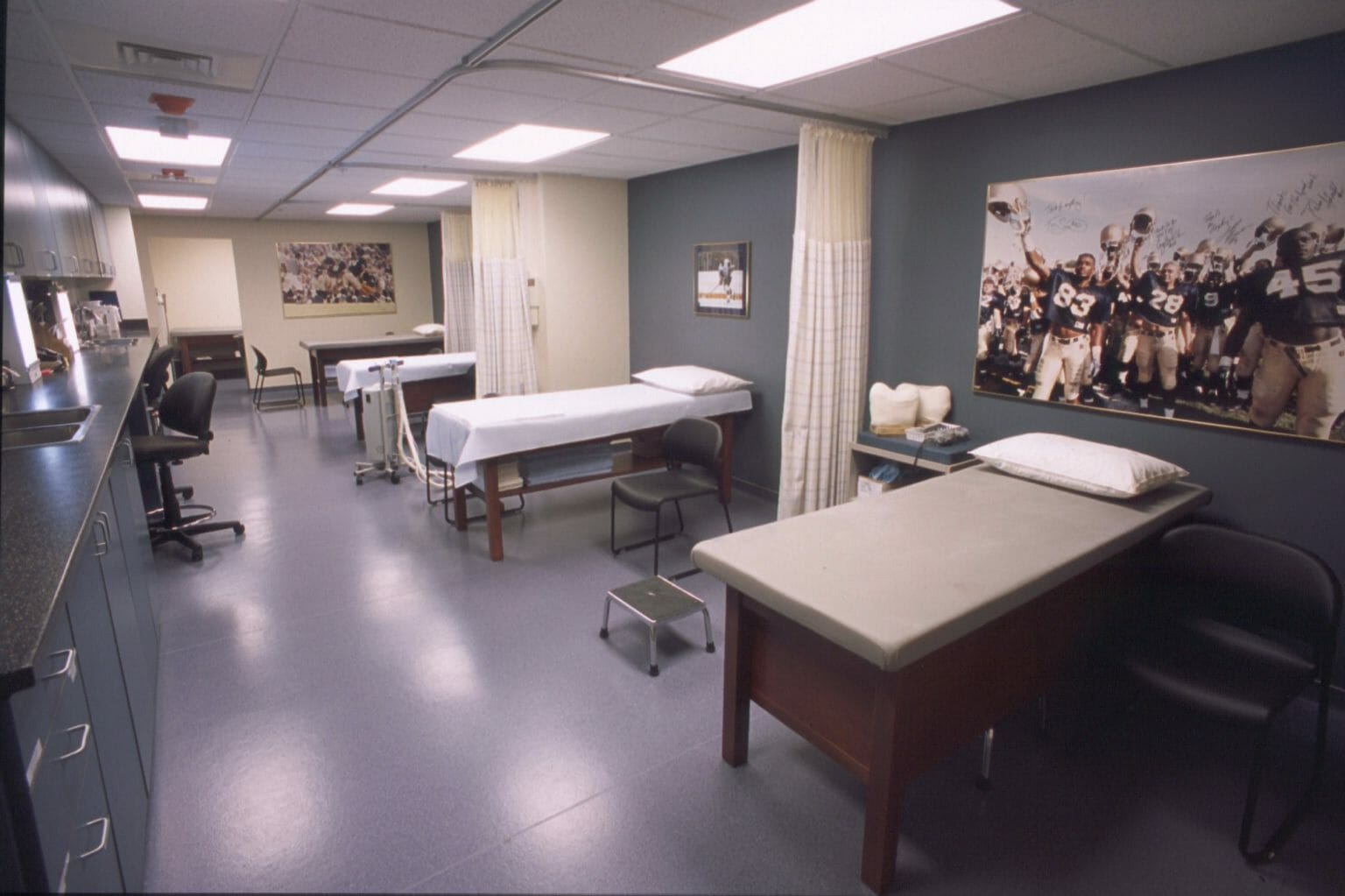 Room with multiple patient beds that are seperated by curtains with sport-related wall décor
