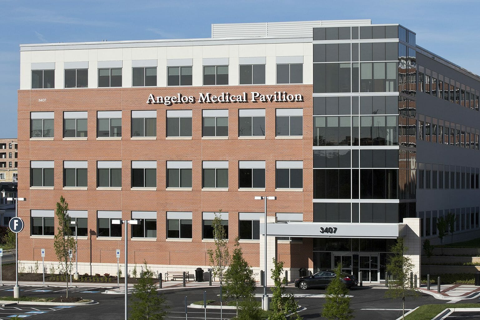 Close-up exterior view of Angelos Medical Pavilion with brick exterior and silver accents with a car in front of the main entrance