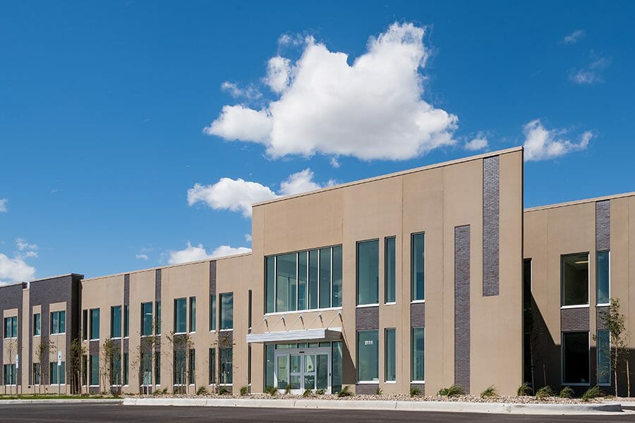 Exterior view of CHI St. Alexius Health with tan stucco and dark brick finishes along with trees planted along the building