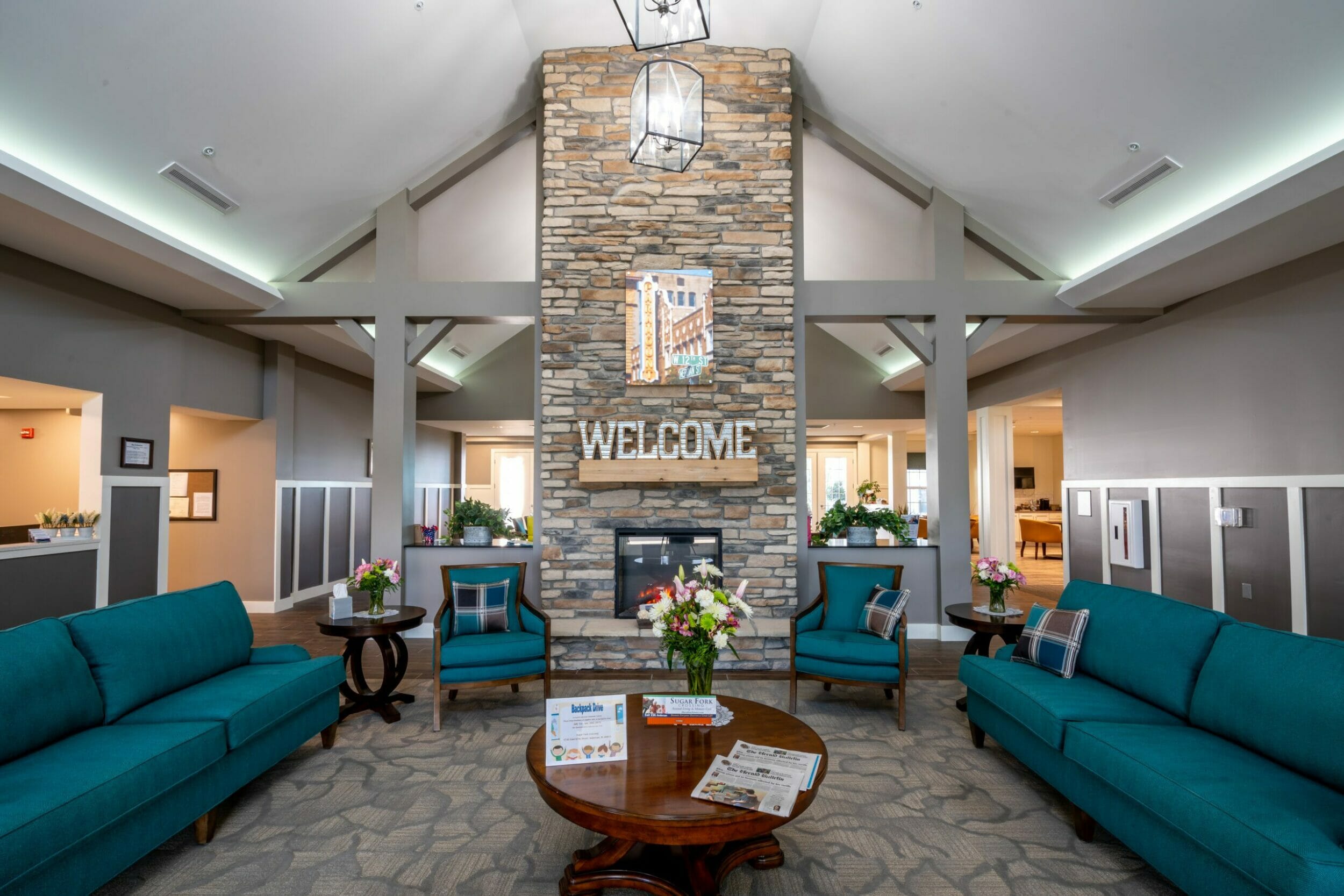 Lounge area of Sugar Fork Crossing senior living with a tall, stone fireplace, gray-colored walls, and teal furniture
