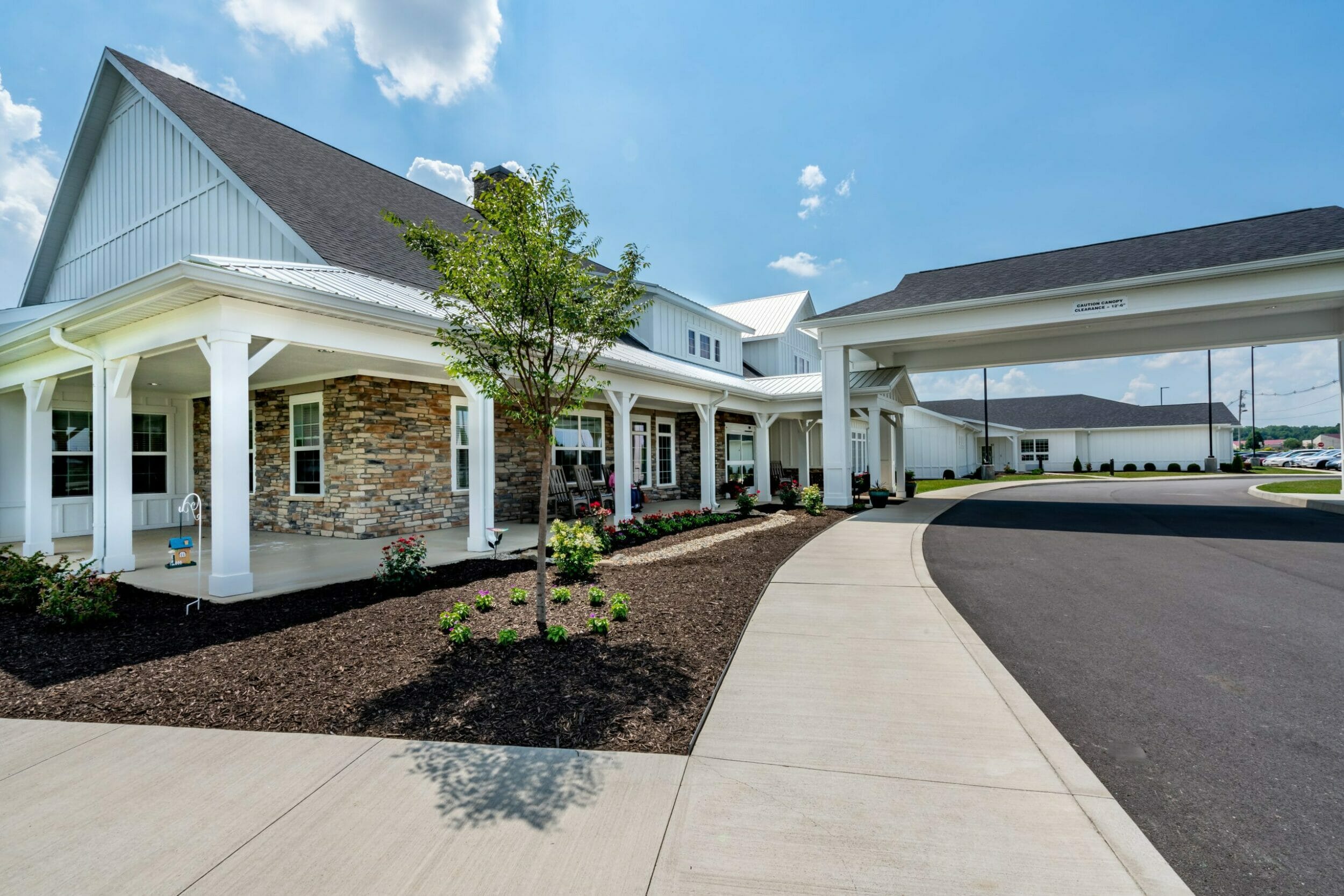 Close-up of front entrance of two-story Sugar Fork Crossing senior living with a white exterior and stone accents with plants around the front of the building