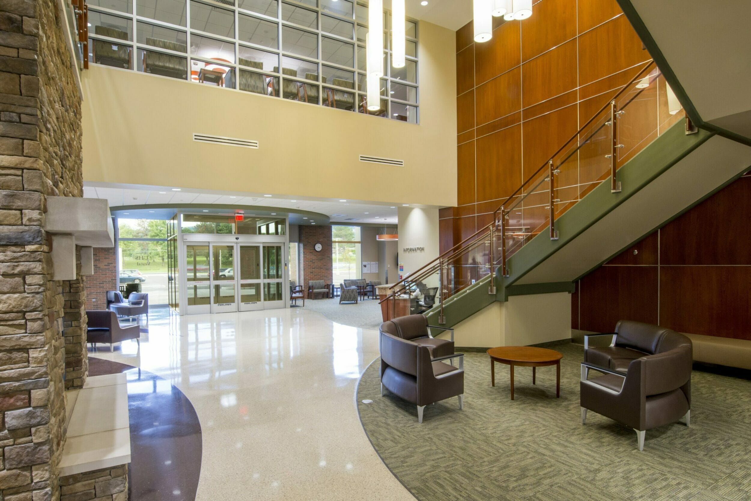 Two-story, medical office lobby looking to the entrance from the inside, with a lounge area by a stone fireplace