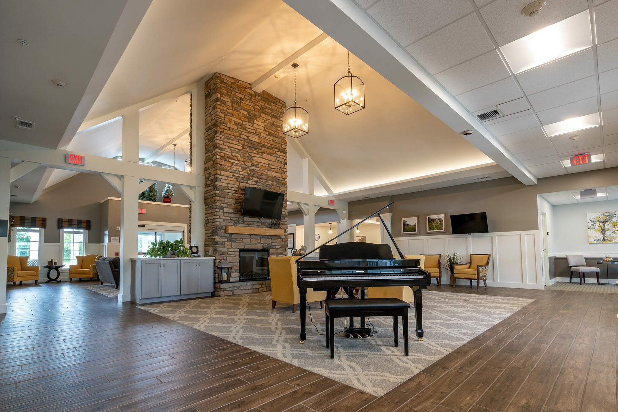 Two-story lobby of Walnut Crossing senior living with grand piano and living room area with fireplace and chairs