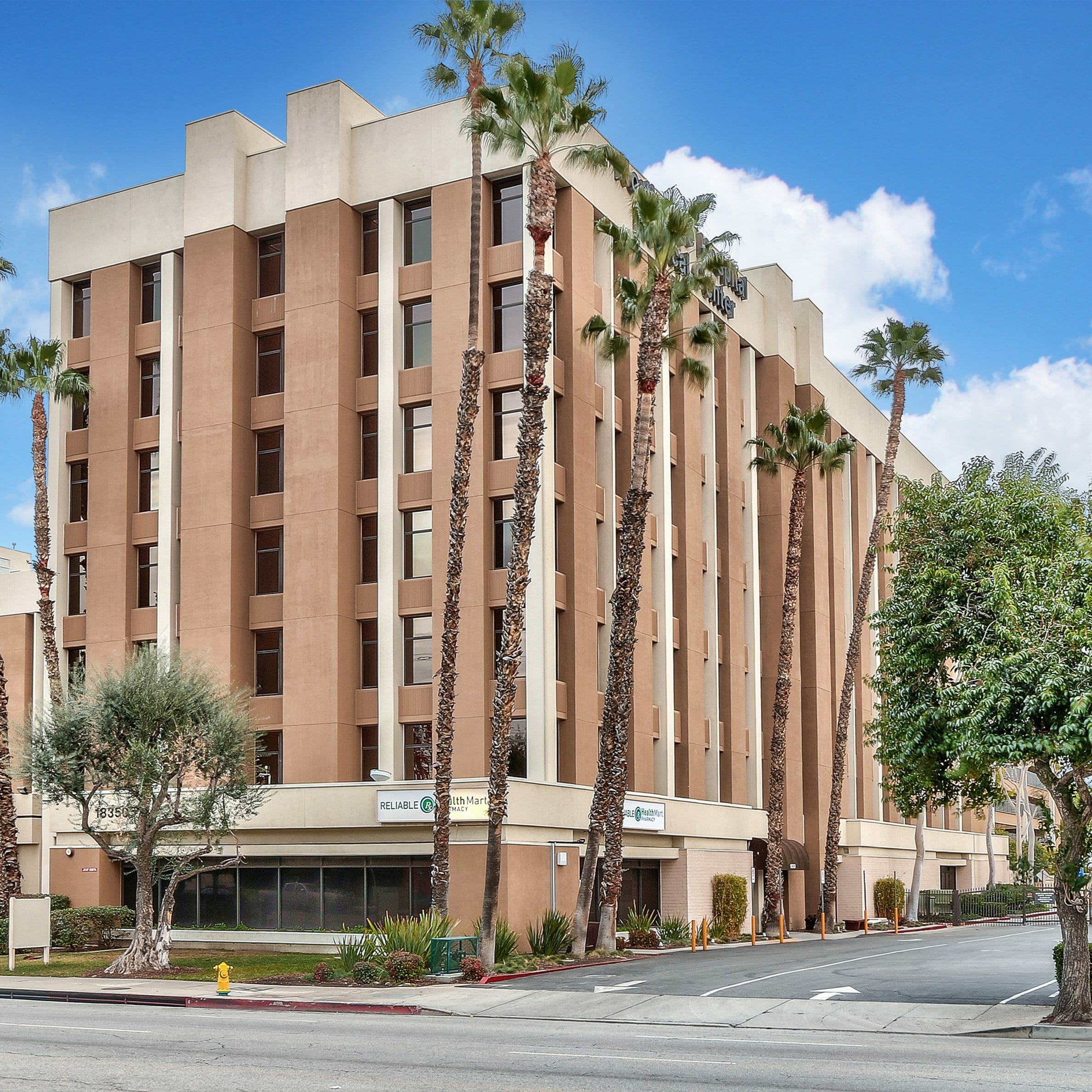 Exterior street view of 7-story medical office building with a medium and light tan exterior with tall, tropical palms in front of the building