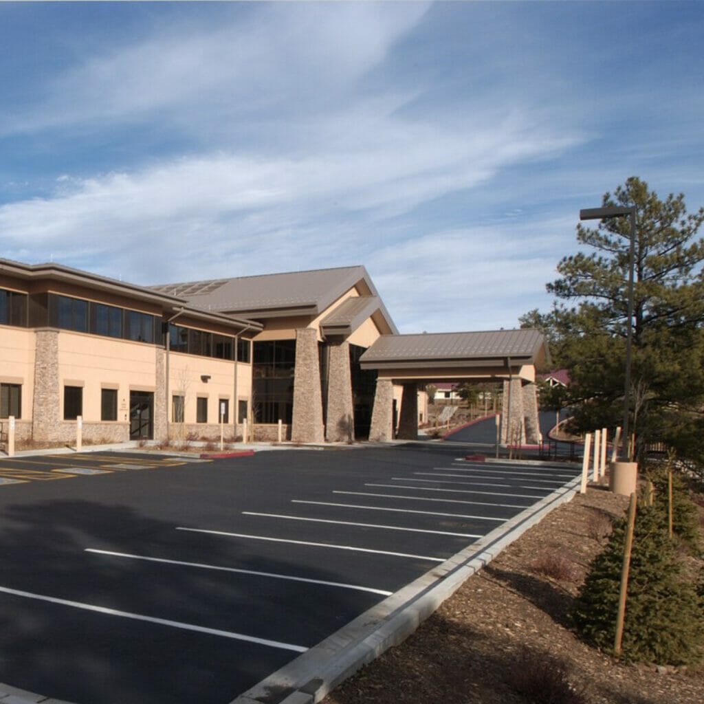 Sideview of the front of a medical office building and parking lot with a stone porte-cochère and a tan stucco exterior