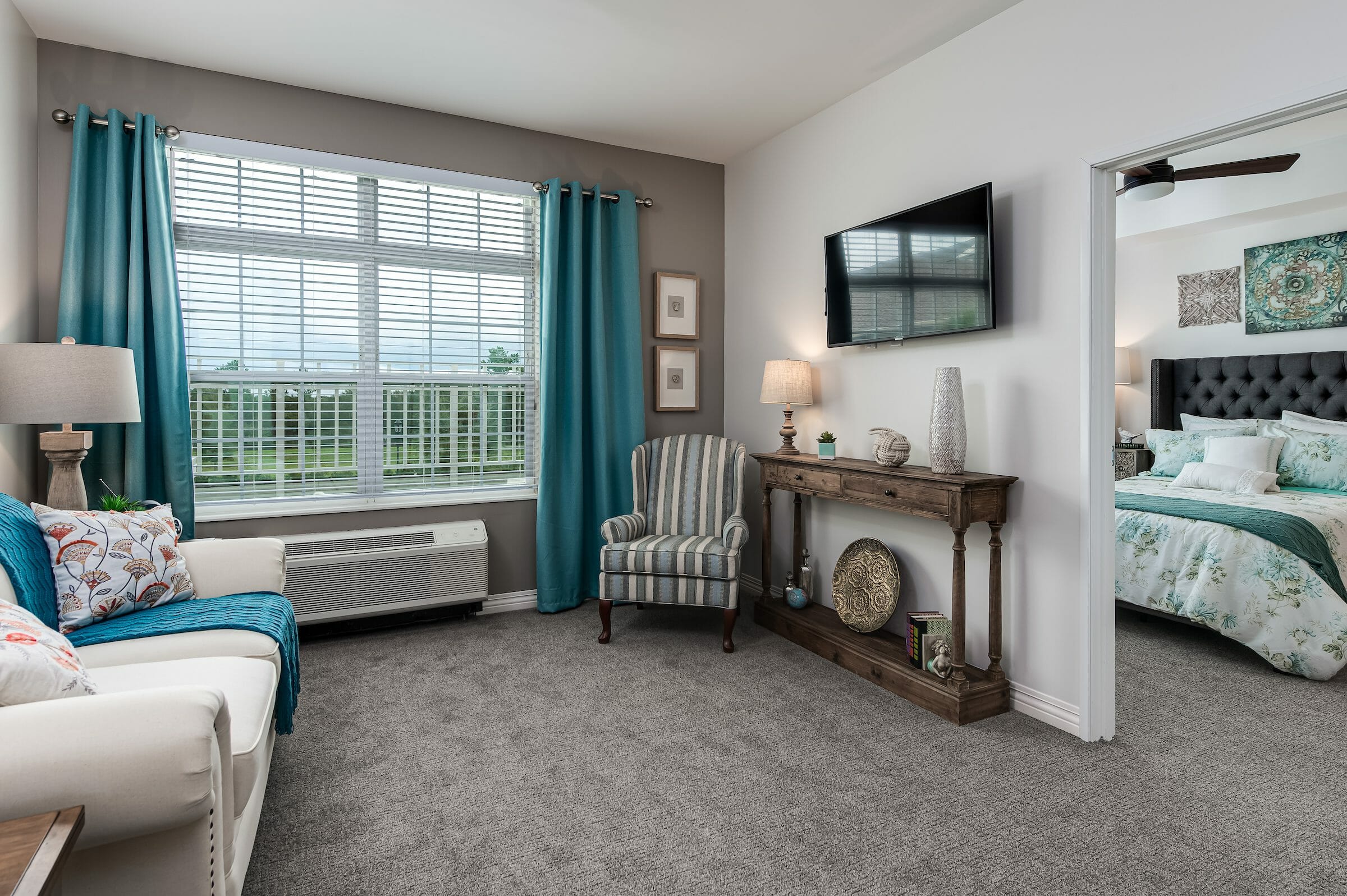 Inside view of a living room and bedroom, both with white, gray and blue accent colors