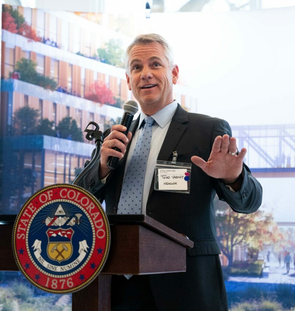 Todd Varney standing behind a podium, holding a microphone, and giving a speech