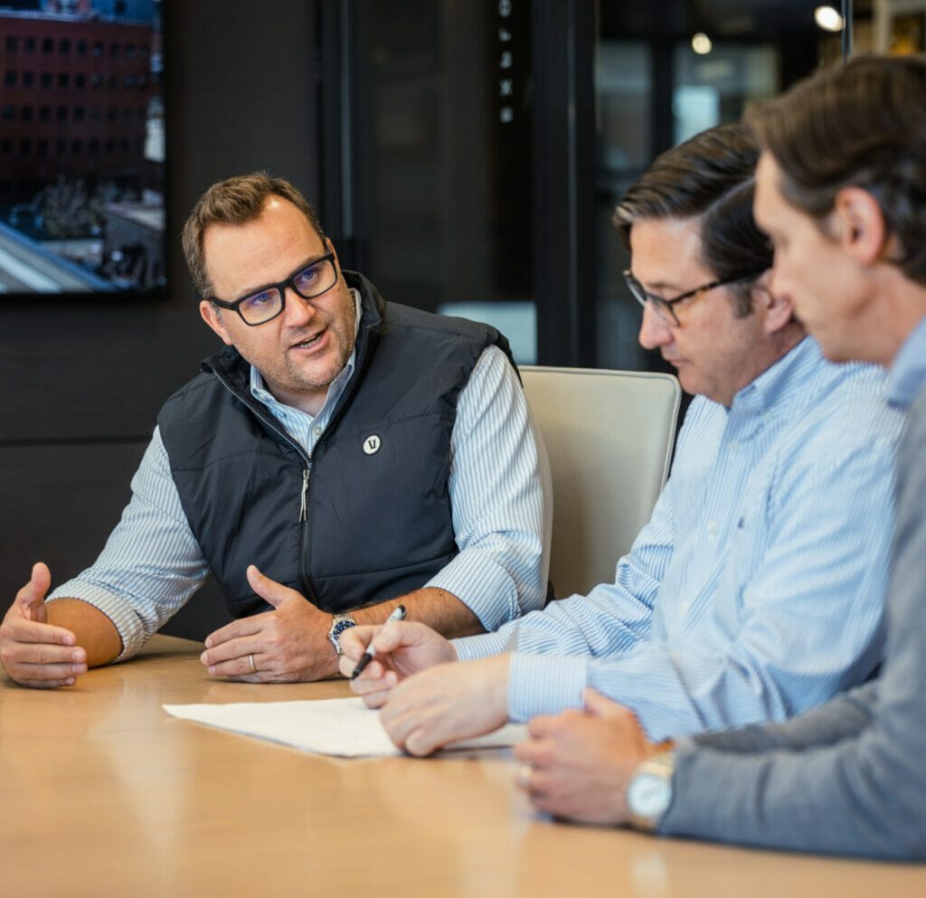 Three men sitting at a conference table discussing a strategy