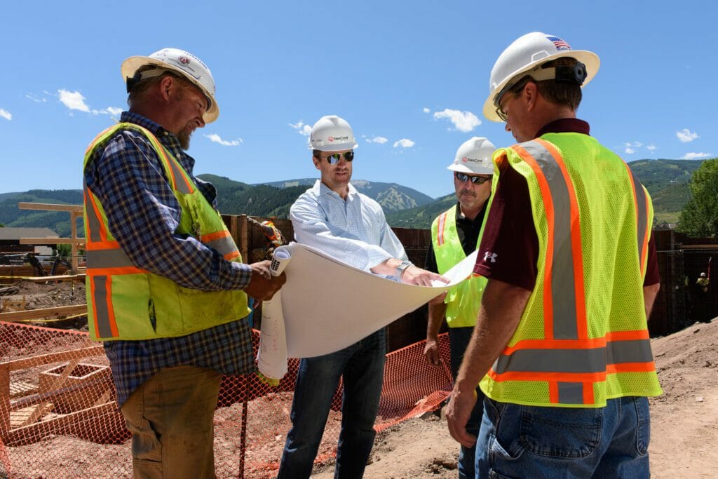 Four men at a construction site, holding blue prints, and discussing the project plans
