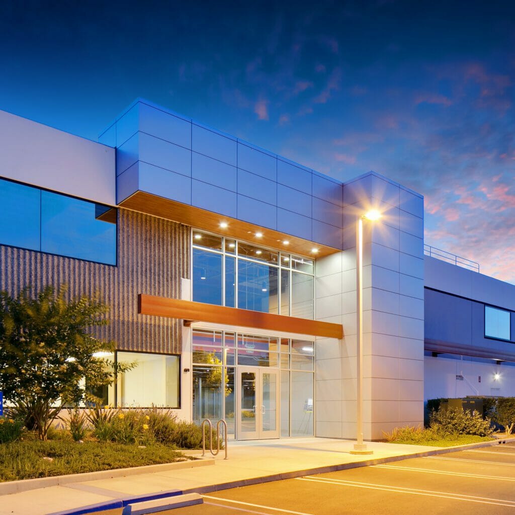 Exterior view of Irive Spectrum at sunset with gray and white exterior finishes with accents of tan wood with parking in front of the building